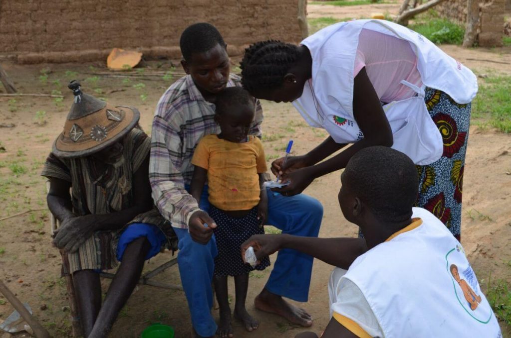 Two African health workers take notes with two African male adults and an African child.