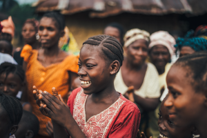 A crowd of African woman, focusing on one woman who is smiling and clapping.