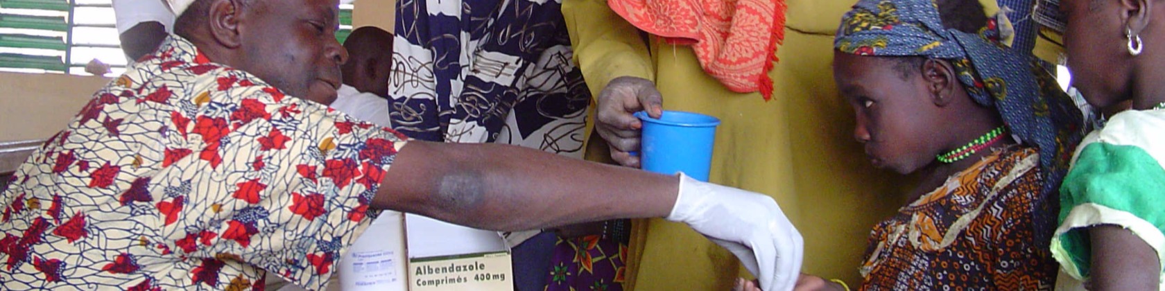 An African medical professional places a deworming pill in an African child's hand.