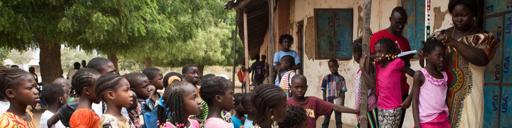 African children waiting in line. An African woman is studying an African child's hair.